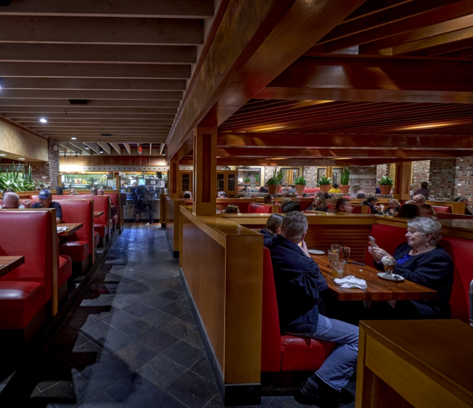 A lively bar scene within a restaurant showcasing patrons engaged in conversation, with a bartender in action and sports broadcasting on overhead televisions.