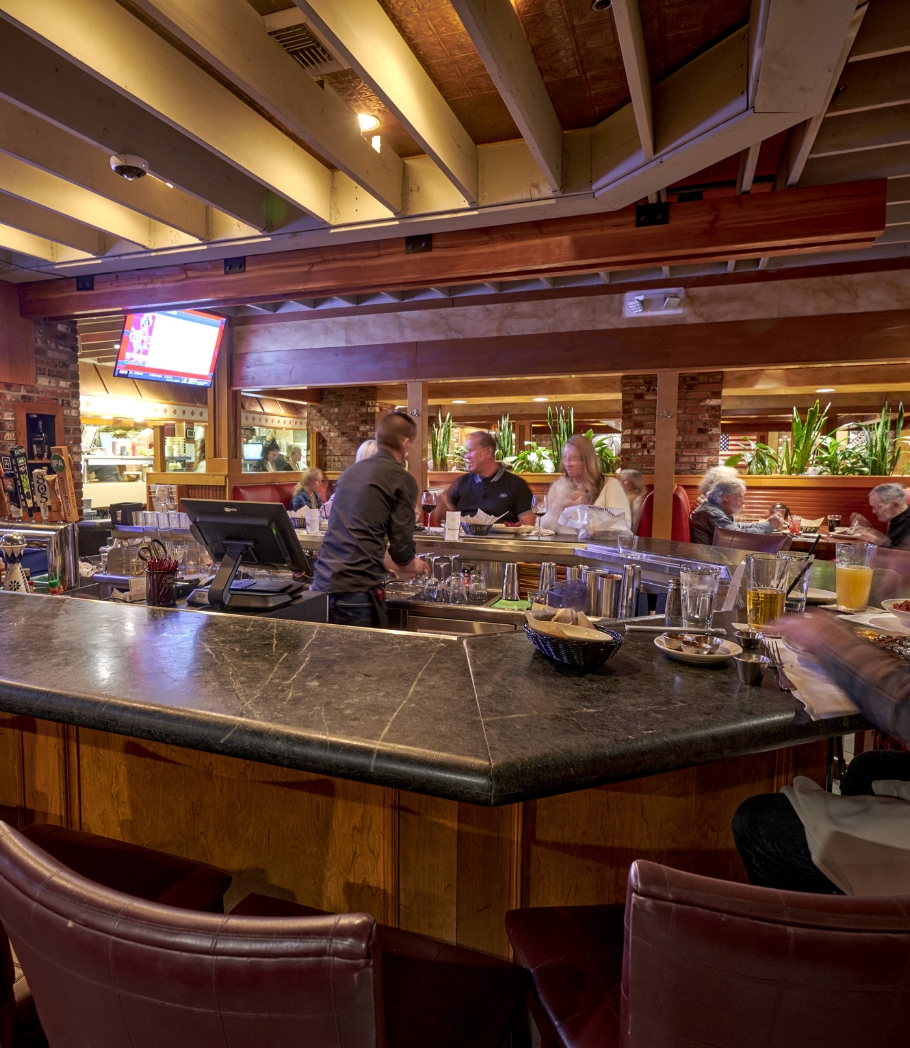 Guests seated at a dining area with red booths and wooden tables, offering a comfortable and intimate setting with overhead wooden beams and ambient lighting.