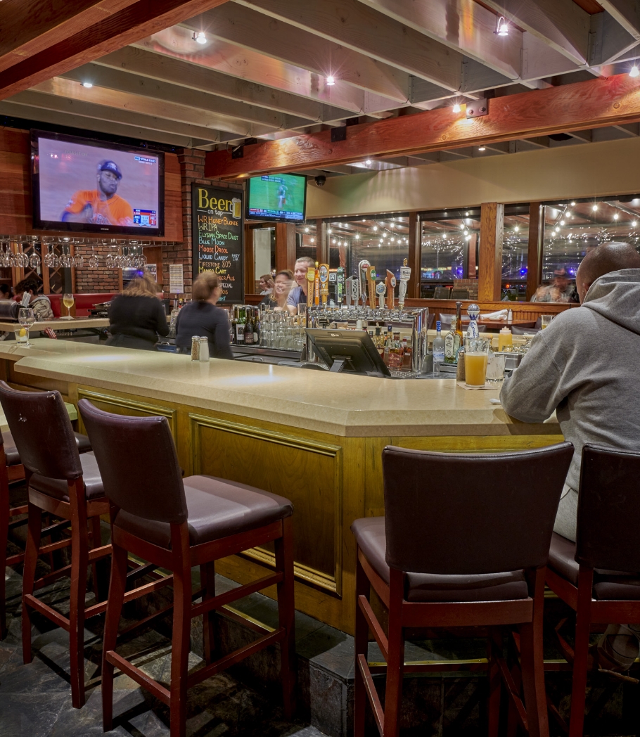 Patrons at a bar with a rustic vibe, sipping drinks and watching a sports game on TV, surrounded by a wooden interior and warm lighting.