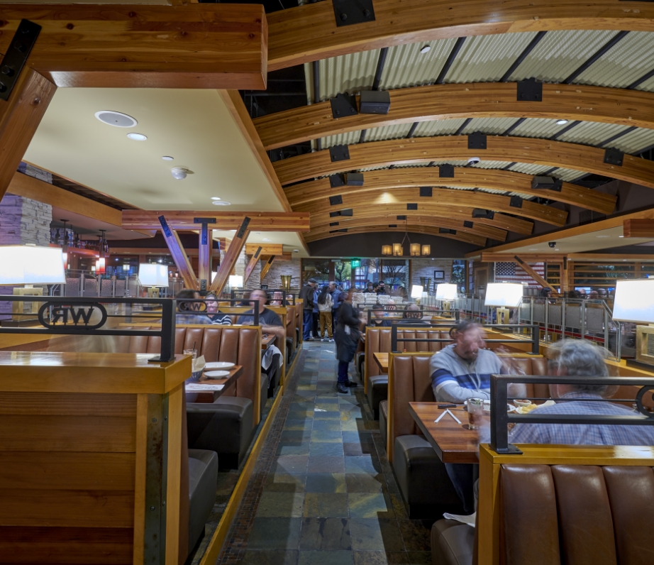 Interior of a cozy restaurant with warm lighting, featuring wooden booths and a vaulted ceiling with exposed beams, capturing the busy ambiance and architectural details.