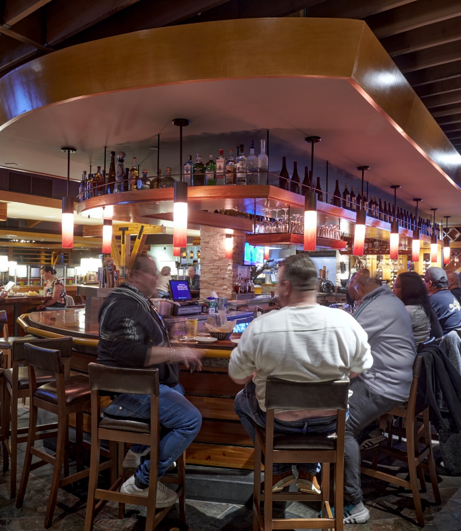 Patrons seated around a circular bar inside a restaurant, with a warm and inviting atmosphere emphasized by overhead mood lighting and a well-stocked bar displaying an array of bottles.