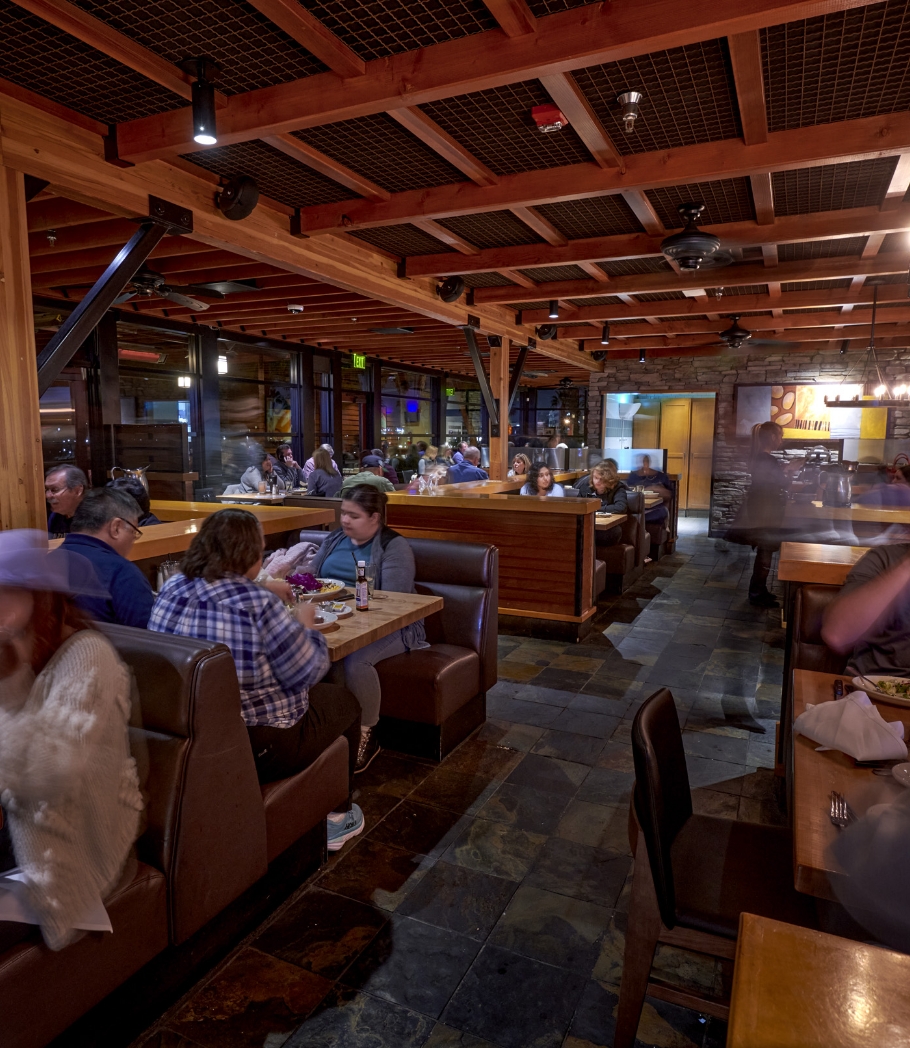 Casual dining scene inside Wood Ranch BBQ & Grill, with guests seated in comfortable booths, enjoying their meals under the warm glow of ceiling lights.