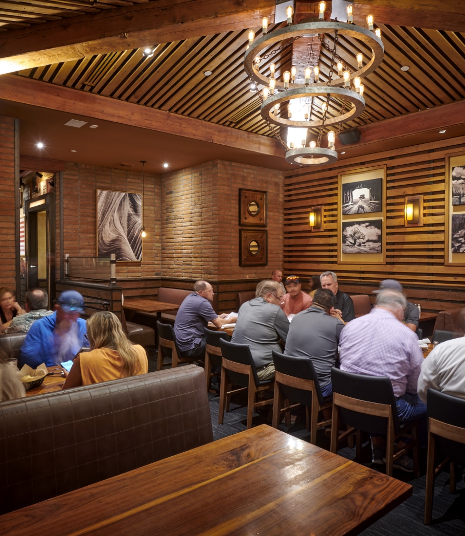 Diners engage in conversation at Wood Ranch BBQ & Grill, seated in comfortable booths under a chandelier that adds a touch of rustic elegance to the wooden and brick interior.