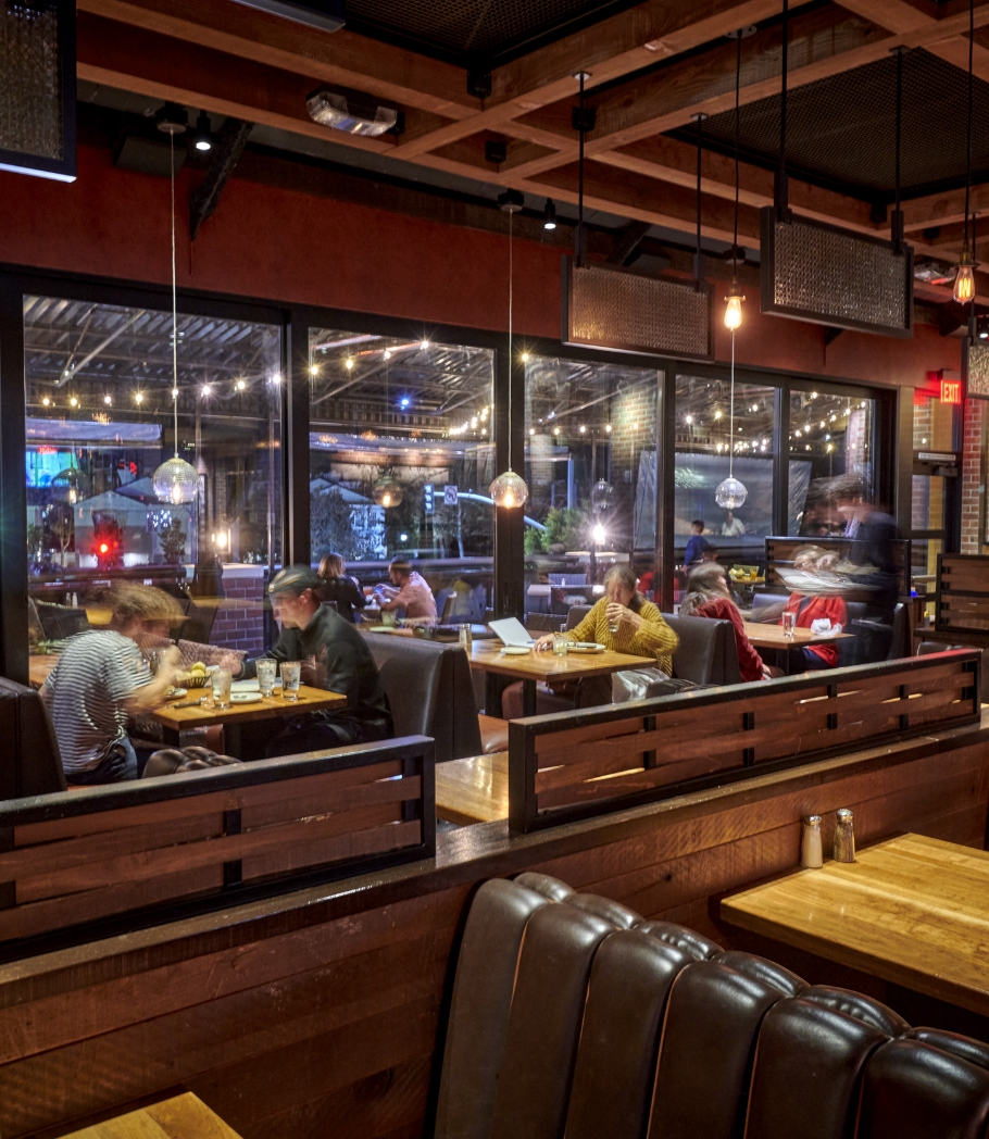 Diners at Wood Ranch BBQ & Grill are seated in a warm, well-lit dining area with large windows providing a view outside, adding to the relaxed and comfortable setting.