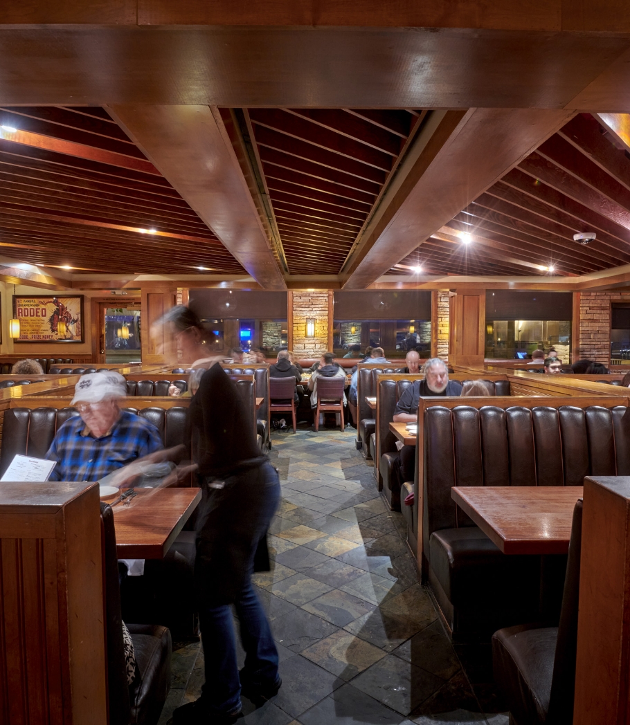 Diners enjoying meals in comfortable booths at Wood Ranch BBQ & Grill in Valencia, with the restaurant's warm wooden interiors and a striking beam ceiling creating a cozy dining experience.