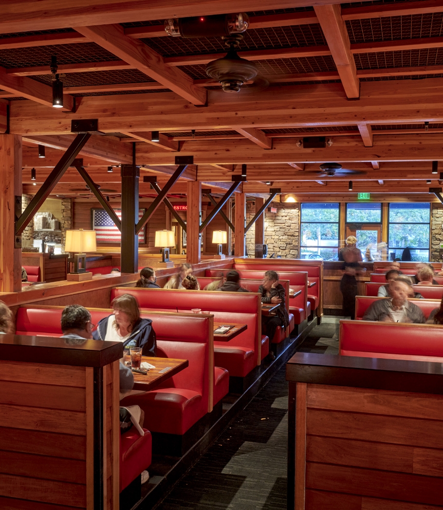 Diners in Wood Ranch BBQ & Grill, Ventura, seated in plush red booths under a ceiling with striking wooden beams, with a warm and inviting ambiance.