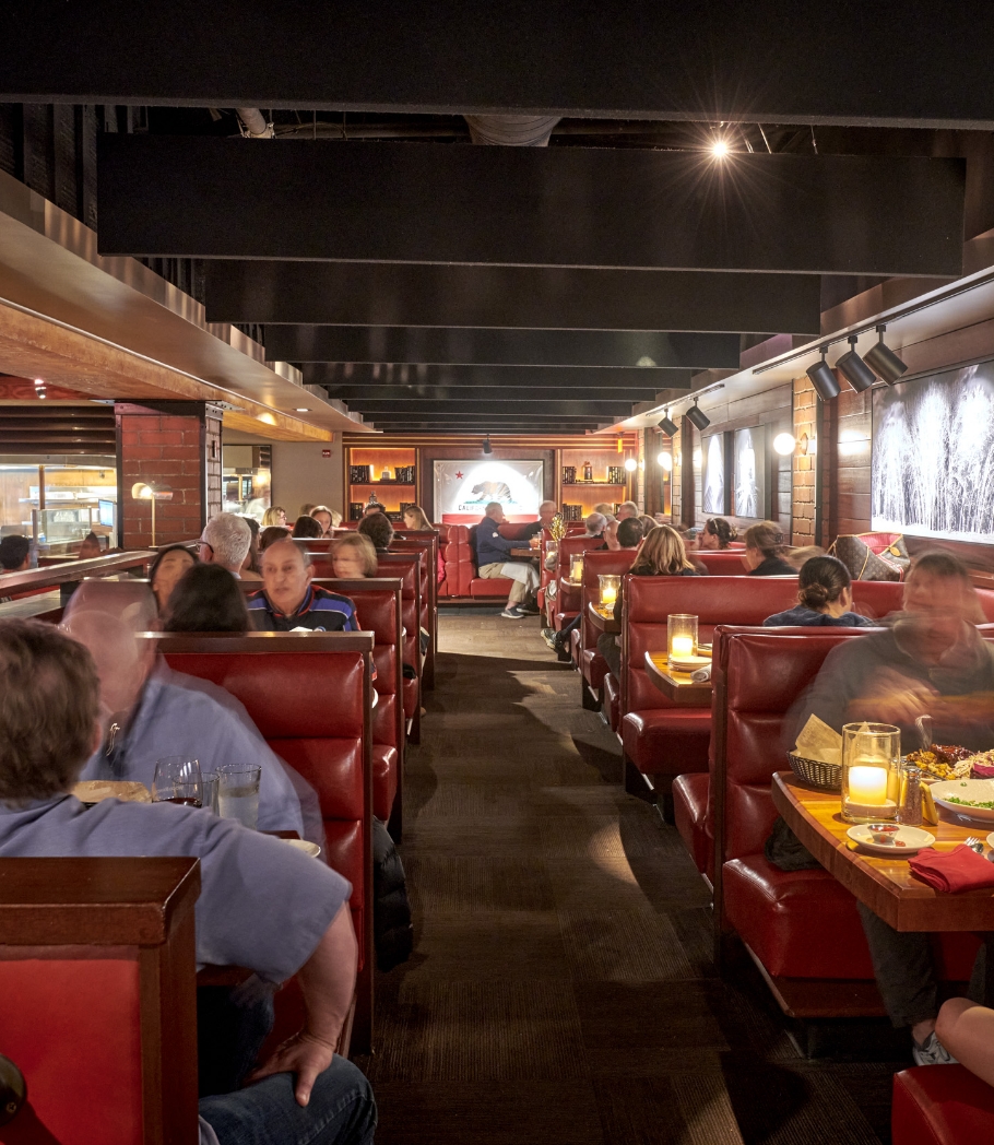 Restaurant patrons seated in red leather booths, dining and conversing in a cozy atmosphere with soft lighting and a classic wooden interior.